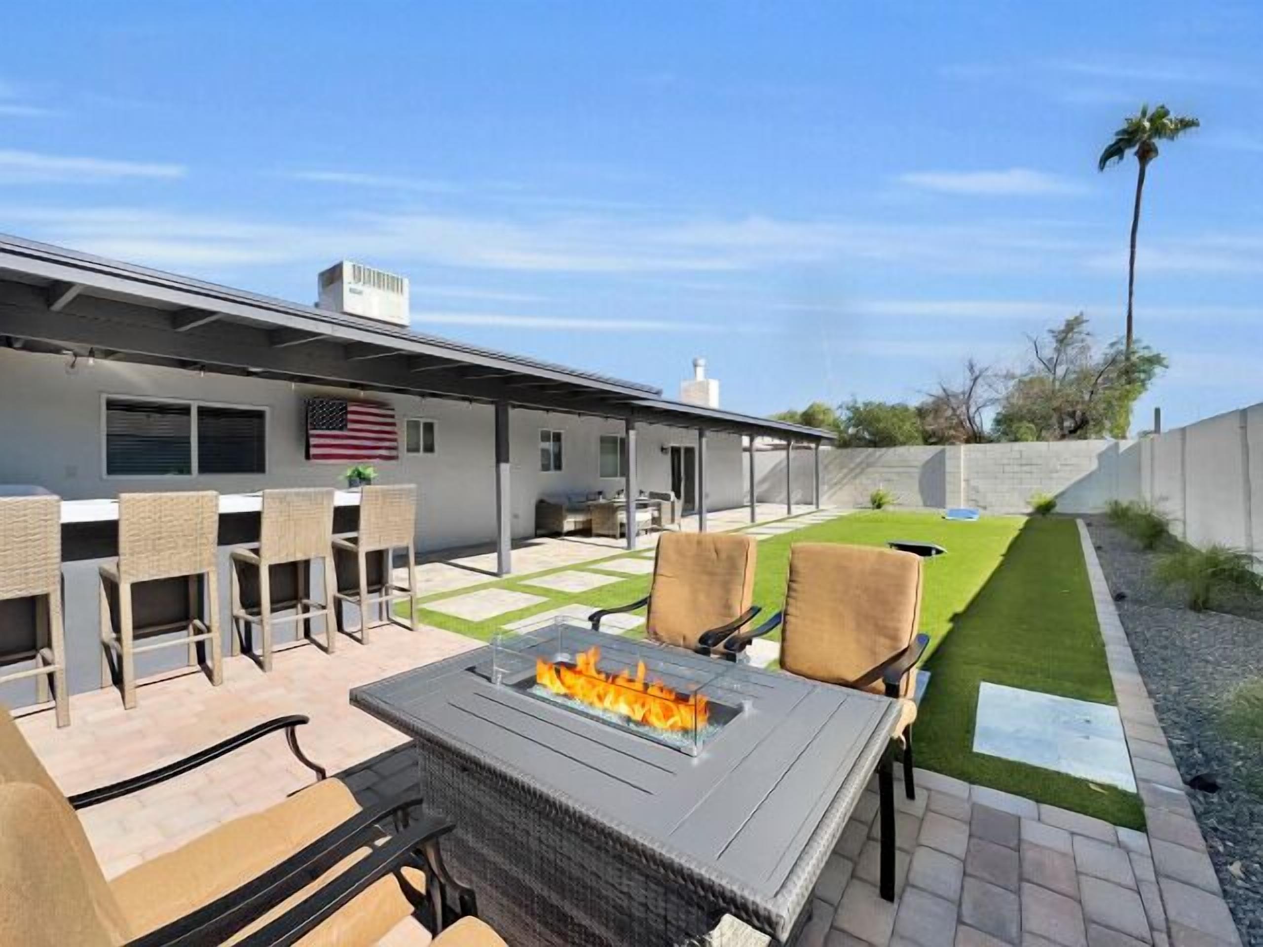 Un patio con una chimenea, mobiliario exterior y un césped cuidado.