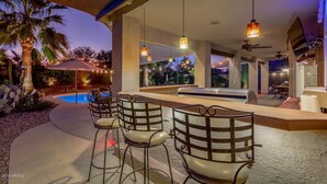 An outdoor bar area with a pool, bar stools, and hanging pendant lights. - Blackfoot San Tan Valley (San Tan Valley)