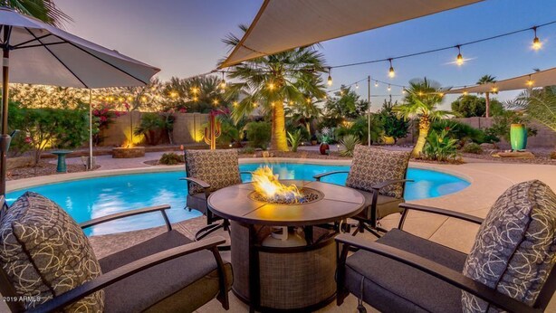 A poolside area with a fire pit table, lounge chairs, and string lights. - Blackfoot San Tan Valley (San Tan Valley)