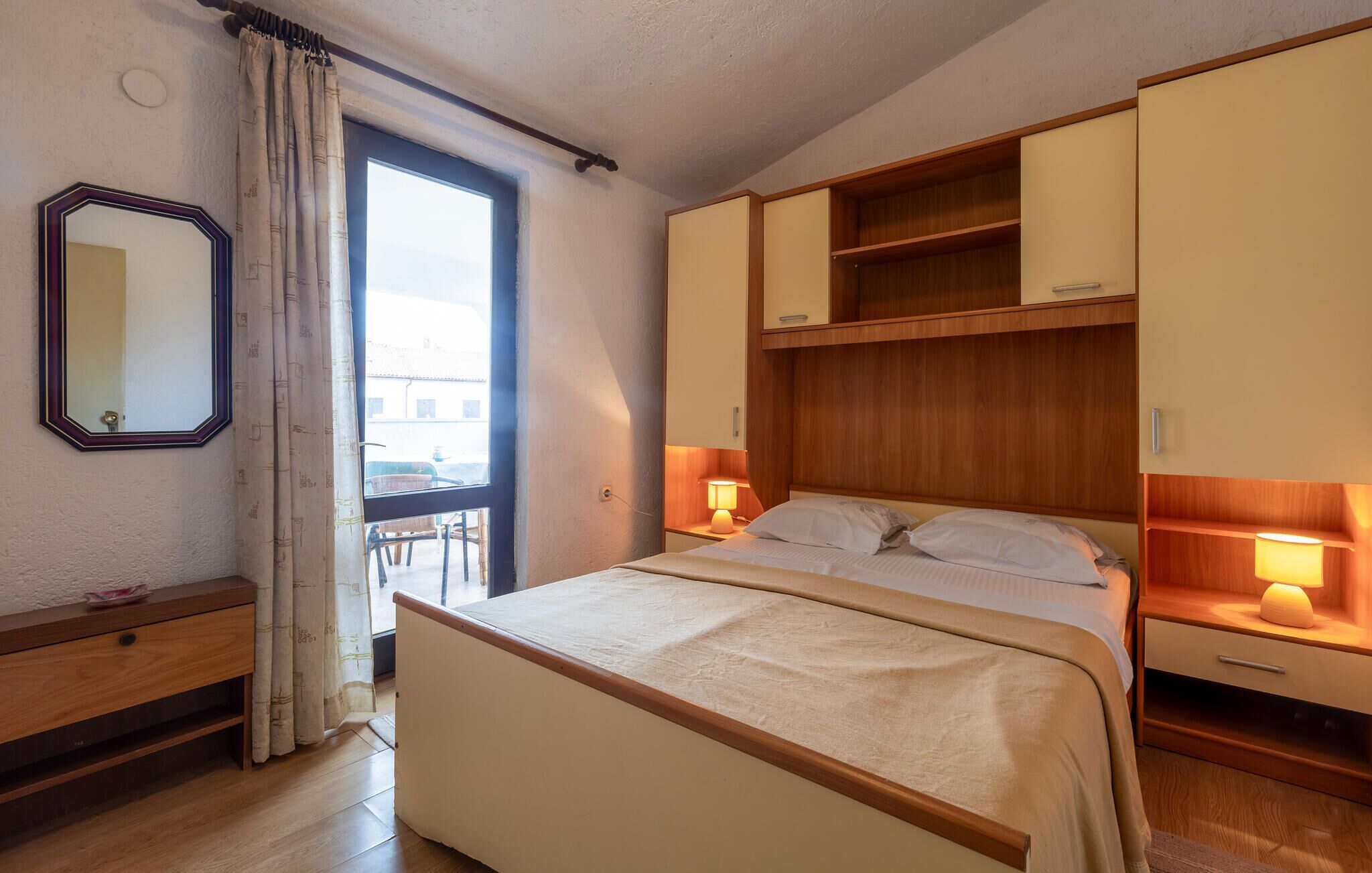 A bedroom with a bed, bedside lamps, a mirror, and a window with curtains.