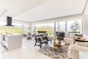 Enjoy a spacious living space with a central seating area, kitchen island, and dining area, offering a view of the surrounding landscape.