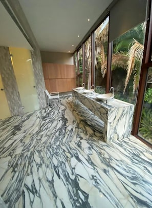Enjoy a refreshing bathroom experience with a bathtub, three sinks, and a view of lush tropical vegetation.