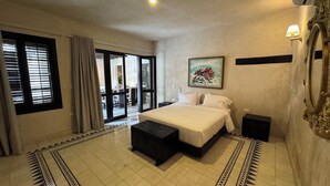 A bedroom with a bed, a nightstand, a dresser, a large window with blinds, and a door leading to a balcony. - Casa Bovedas Collection by Ritzy Group (Cartagena de Indias)