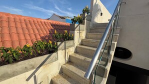 A staircase with a glass railing leading to a landing, surrounded by potted plants and a red-tiled roof. - Casa Bovedas Collection by Ritzy Group (Cartagena de Indias)