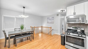 Una cocina moderna con comedor, suelo de madera, armarios blancos y una estufa de acero inoxidable.