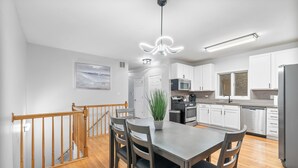 Una cocina moderna con armarios blancos, un refrigerador de acero inoxidable y un comedor con mesa y sillas de madera.