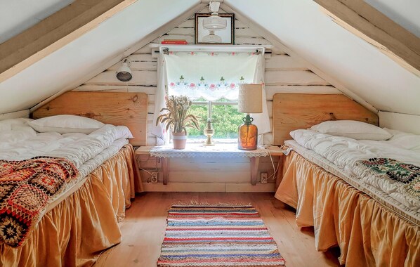 A cozy attic bedroom with two beds, a window with a view, a lamp, and a small table with a plant.