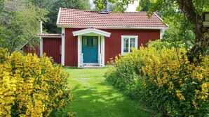 A red house with a green door, surrounded by yellow flowers and green grass. - Pet friendly home in Malmbäck with WiFi (Malmbäck)