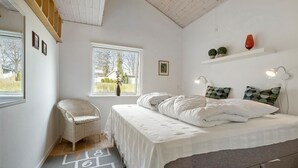 Ein Schlafzimmer mit Bett, Sessel, Fenster, Ablagefläche mit Dekoration und einer Wandlampe.