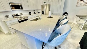 A modern kitchen with white cabinetry, stainless steel appliances, and a central island with bar stools.