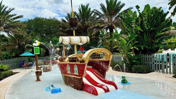 A pirate ship water slide in a tropical setting with palm trees and a wooden fence in the background.