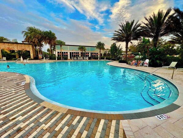 A large outdoor swimming pool with a curved edge, surrounded by lounge chairs and palm trees.