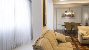 A modern living room with a beige sofa, a dining area with a chandelier, and a large window with sheer curtains. - ROCK IN RIO 2026 PROMO Sep 5th to 14th
Best Location Best Living in Rio. (Rio de Janeiro)