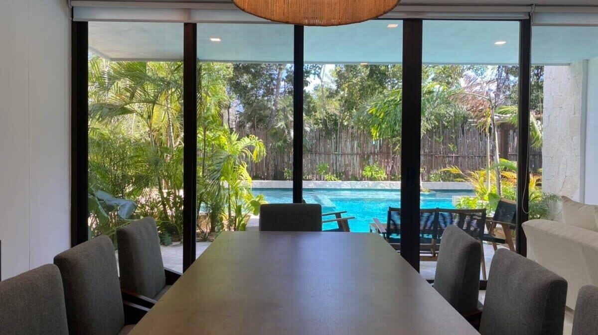 Une salle de conférence dotée d’une grande table et de chaises, offrant une vue sur une piscine et une végétation luxuriante.
