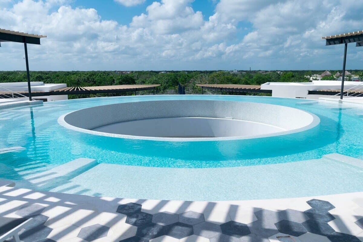 A circular infinity pool with a clear blue edge, surrounded by lounge chairs and a tiled deck.