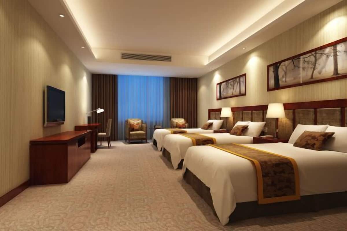 A hotel room with a large bed, two smaller beds, a desk, a chair, a TV, and a window with curtains.
