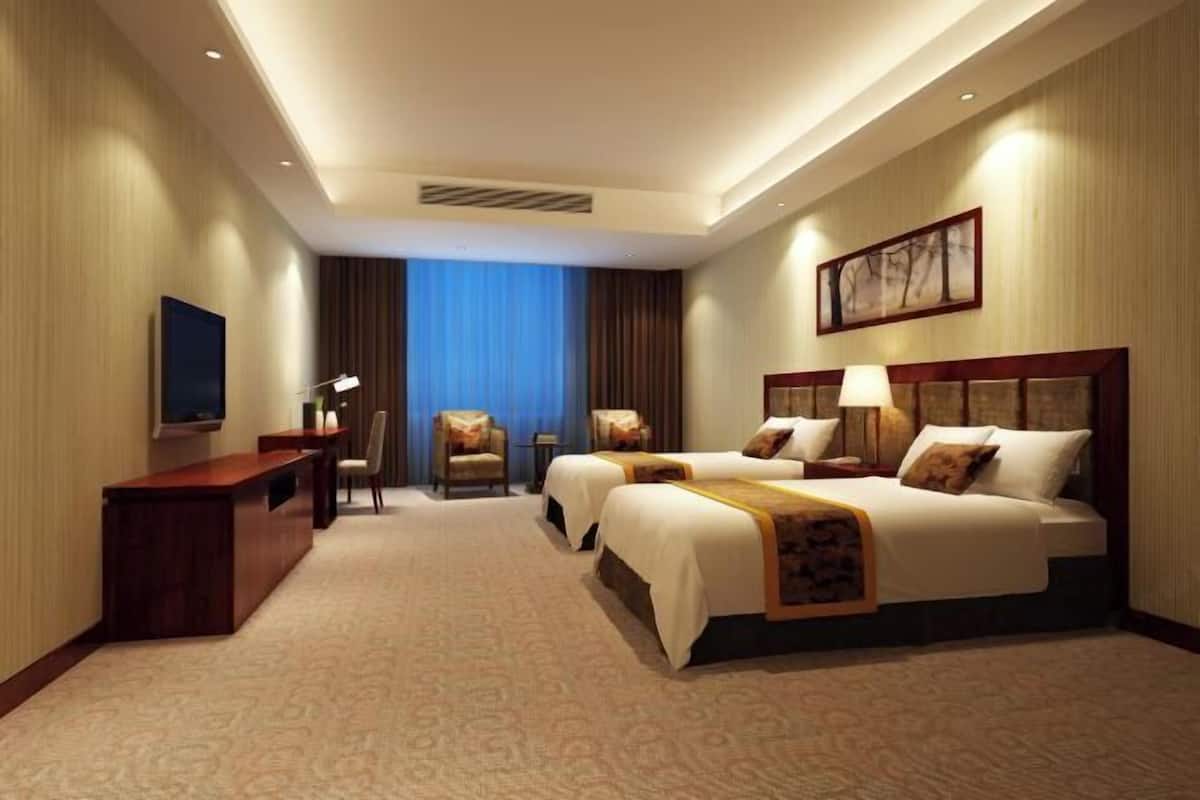 A hotel room with a large bed, a desk, a chair, a TV, and a window with curtains.