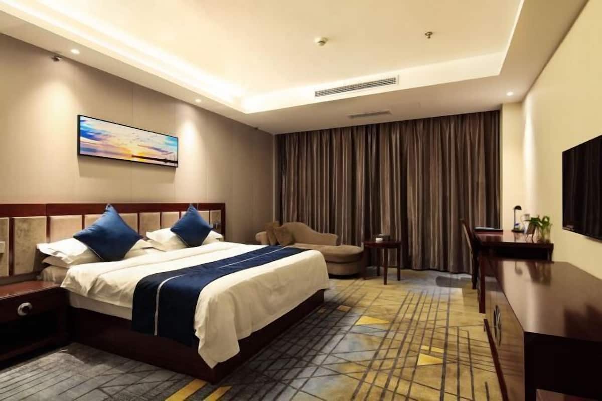 A hotel room with a bed, a desk, a chair, a TV, and a painting on the wall.