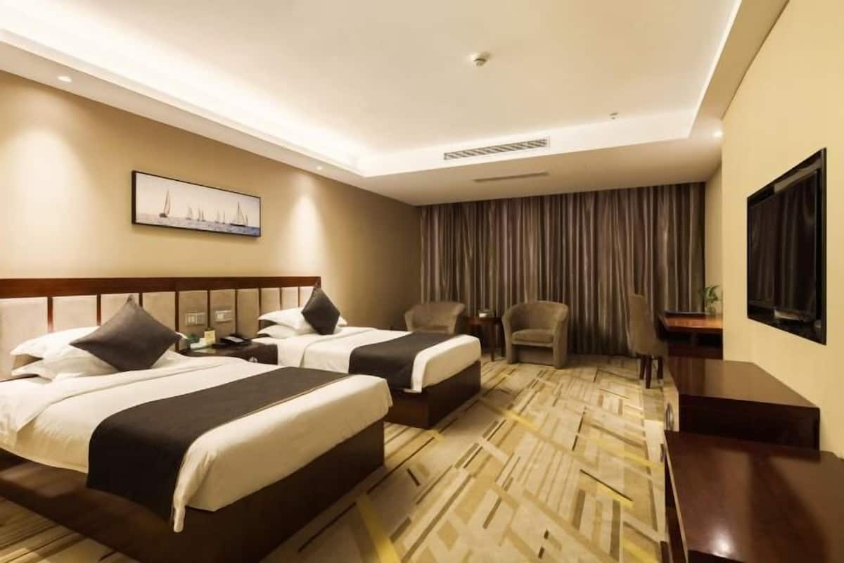 A hotel room with two beds, a desk, a chair, a television, and a painting on the wall.