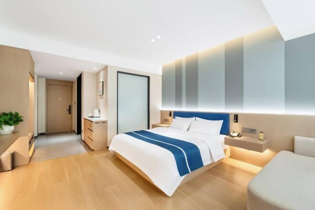 A modern hotel room with a large bed, bedside tables, a nightstand, and a wall-mounted light fixture.