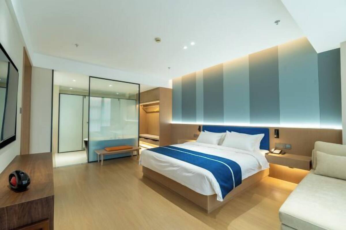 A modern hotel room with a large bed, bedside tables, a desk, and a seating area.