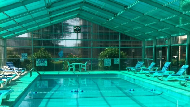 Ein Hallenbad mit überdachtem Dach, mehreren Bahnen und Liegestühlen am Rand.