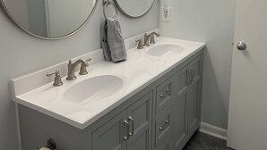 Ein Badezimmer mit zwei Waschbecken, einem Handtuchhalter, einem Toilettenpapierhalter und einer Tür.