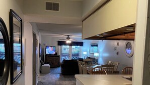 Eine moderne Küche mit einer zentralen Kochinsel, ein Essbereich mit Stühlen und ein Wohnzimmer mit Sofa und Fernseher.