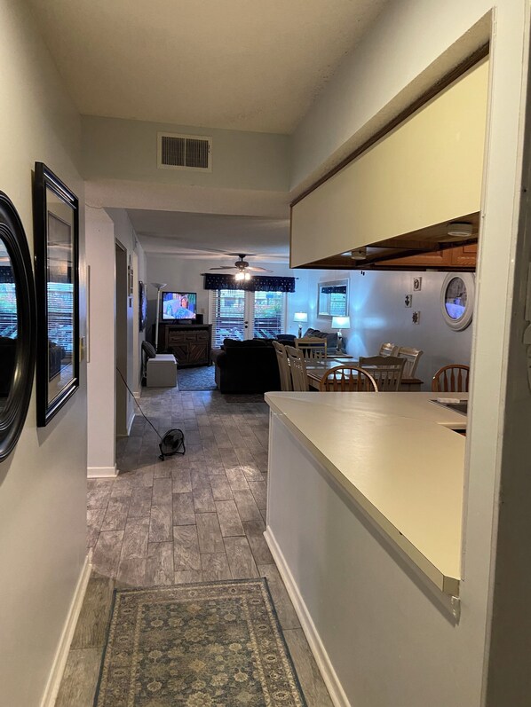 A modern kitchen with a central island, a dining area with chairs, and a living room with a sofa and TV. - Best Little Secret in Myrtle Beach, 2 Bedroom 2 Bath Condo Ground Floor Unit (Myrtle Beach)