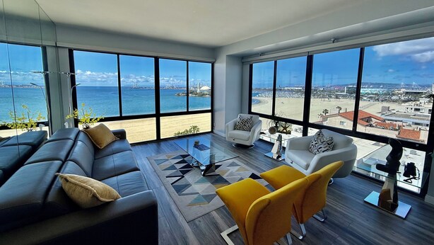 Ein geräumiges Wohnzimmer mit großem Fenster, das Blick auf Strand und Stadt bietet.
