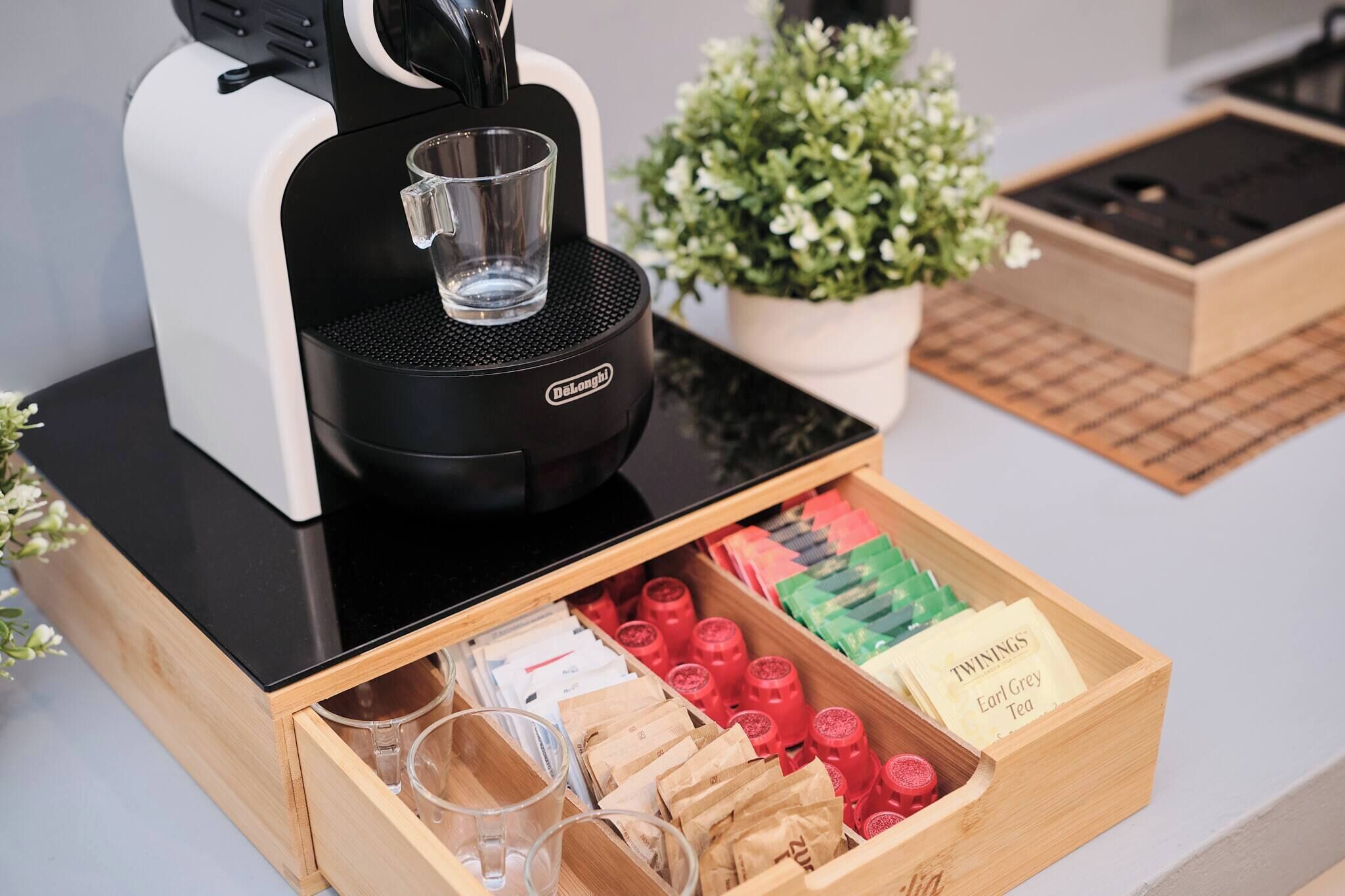A coffee machine with a drawer containing tea bags and glasses.
