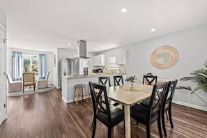 A modern kitchen with a central island, dining area with chairs, and a large mirror on the wall.