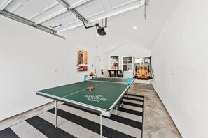 A ping pong table in a room with a high ceiling and a view of a red car through a window.