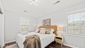 Une chambre à coucher comprenant un lit, des lampes de chevet, une tête de lit, une fenêtre avec des stores et un luminaire au plafond.