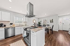 A modern kitchen with white cabinetry, a central island, a built-in oven, and a stainless steel dishwasher.