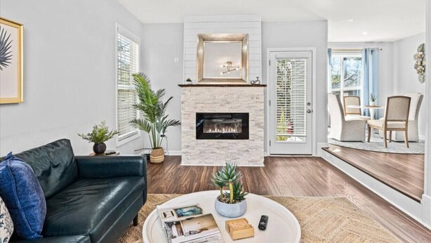 Un salon moderne avec une cheminée, un canapé en cuir noir, une table basse avec des livres et une plante, et un coin repas avec des chaises et une table.