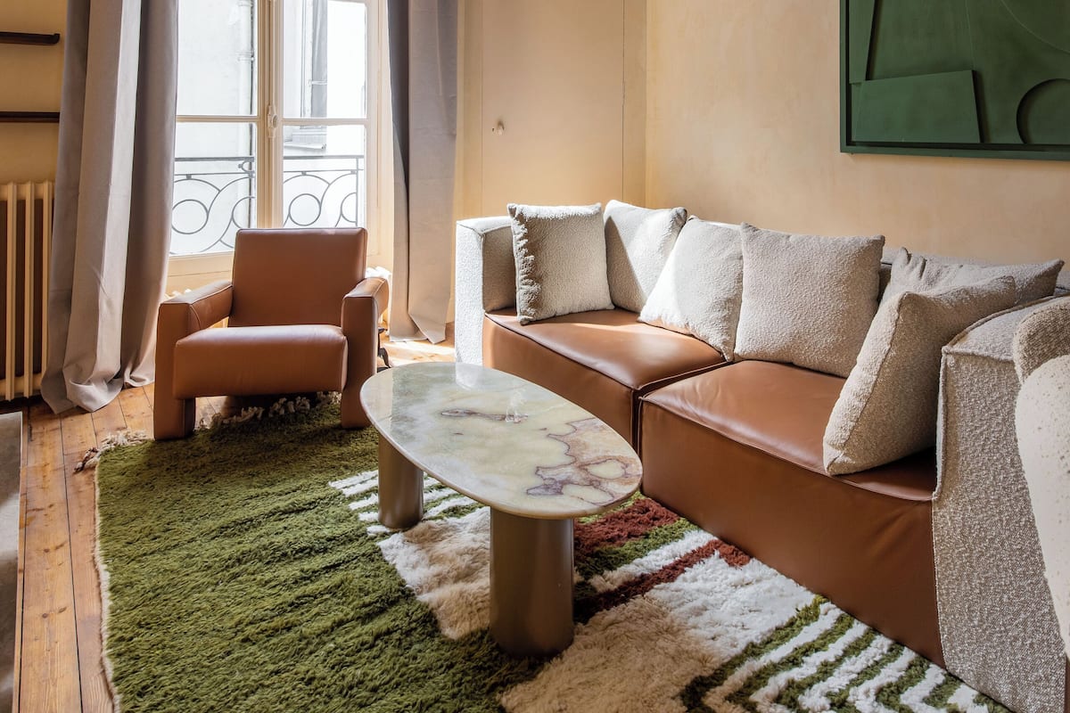 A living room with a sofa, armchairs, a coffee table, and a large window with curtains.