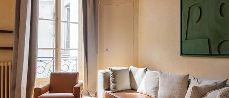A living room with a sofa, armchairs, a coffee table, and a large window with curtains.
