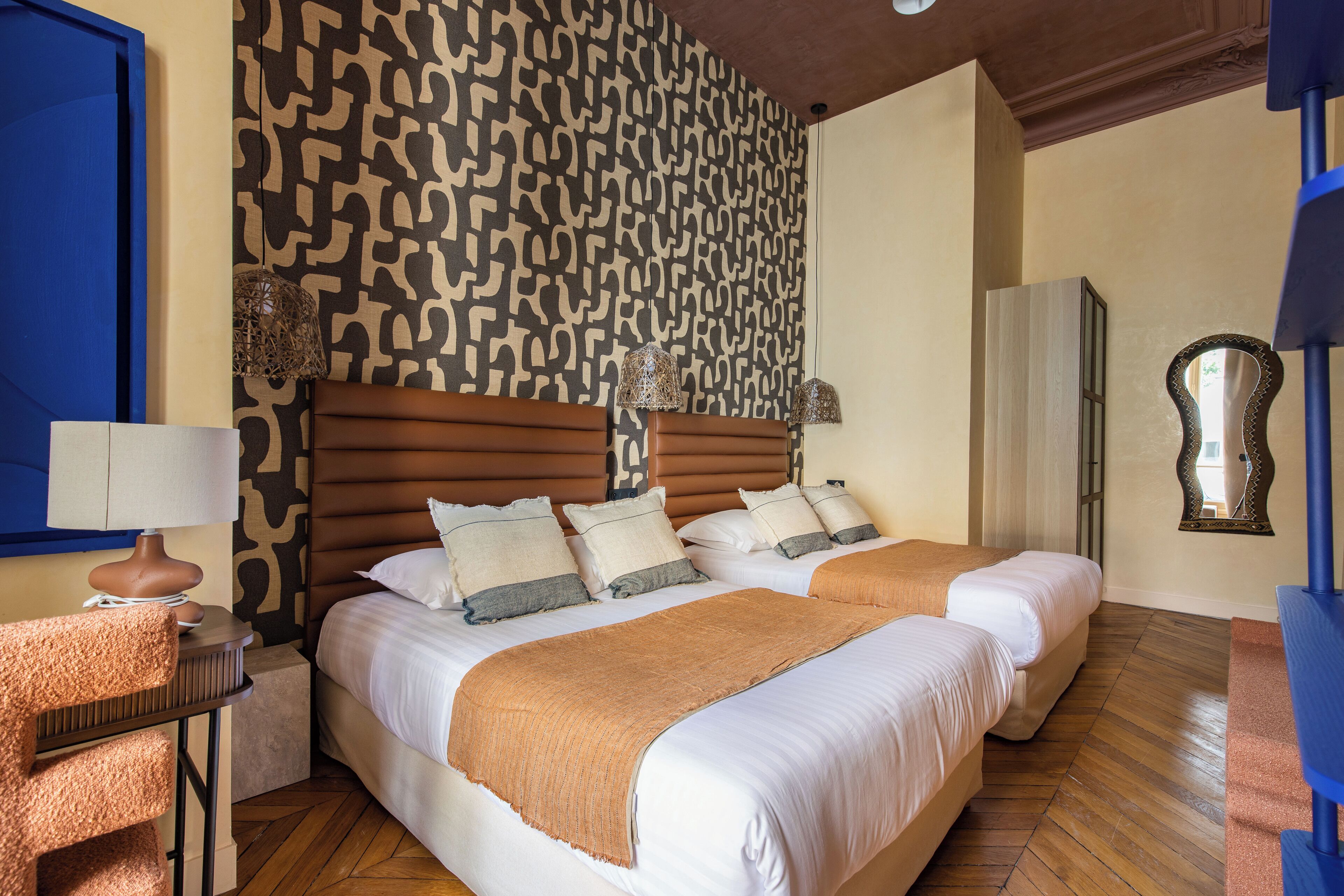 Ein Hotelzimmer mit zwei Betten, einer gemusterten Wand, einem Holzboden und einem Spiegel.
