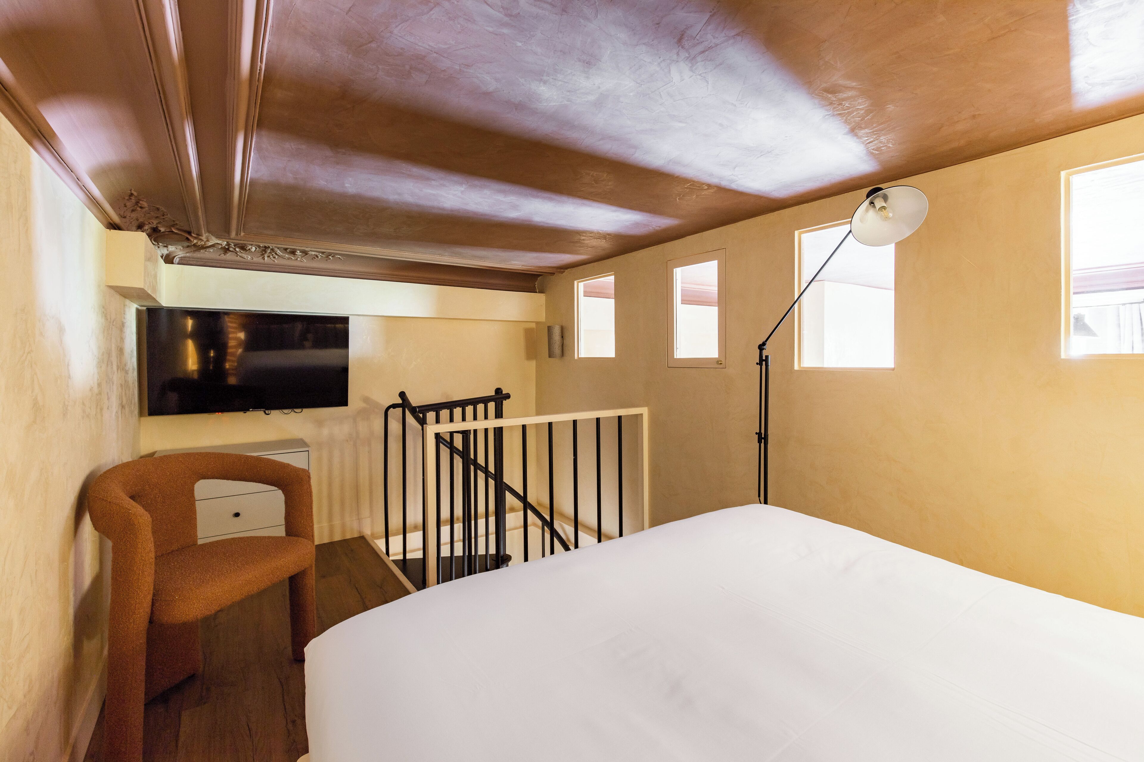 A bedroom with a bed, a chair, a desk, a TV, and a staircase.
