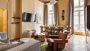A living room with a sofa, armchairs, a coffee table, a TV, and a dining area with chairs and a table. - Hotel My Paris - Grands Boulevards (Paris)