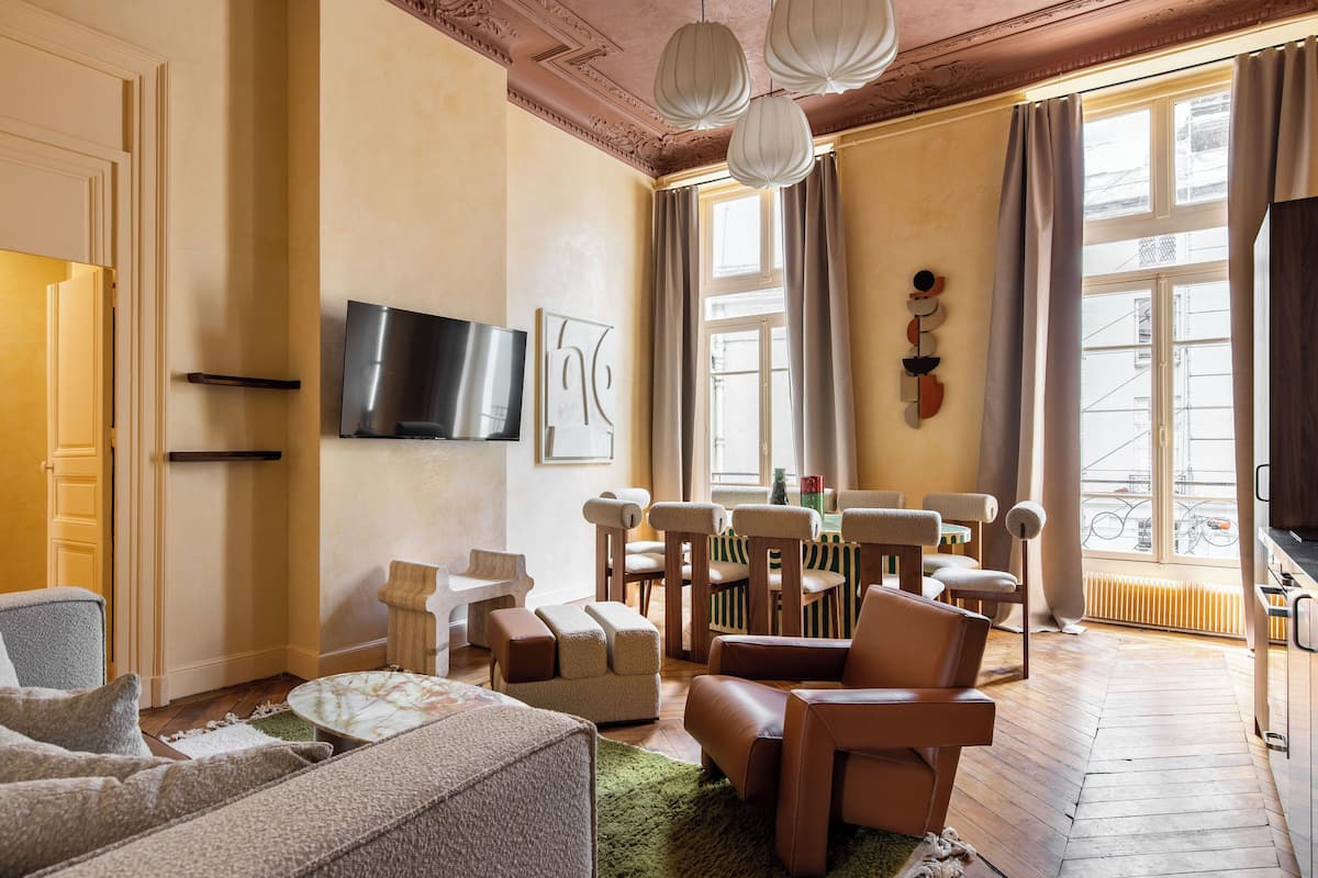 A living room with a sofa, armchairs, a coffee table, a TV, and a dining area with chairs and a table.