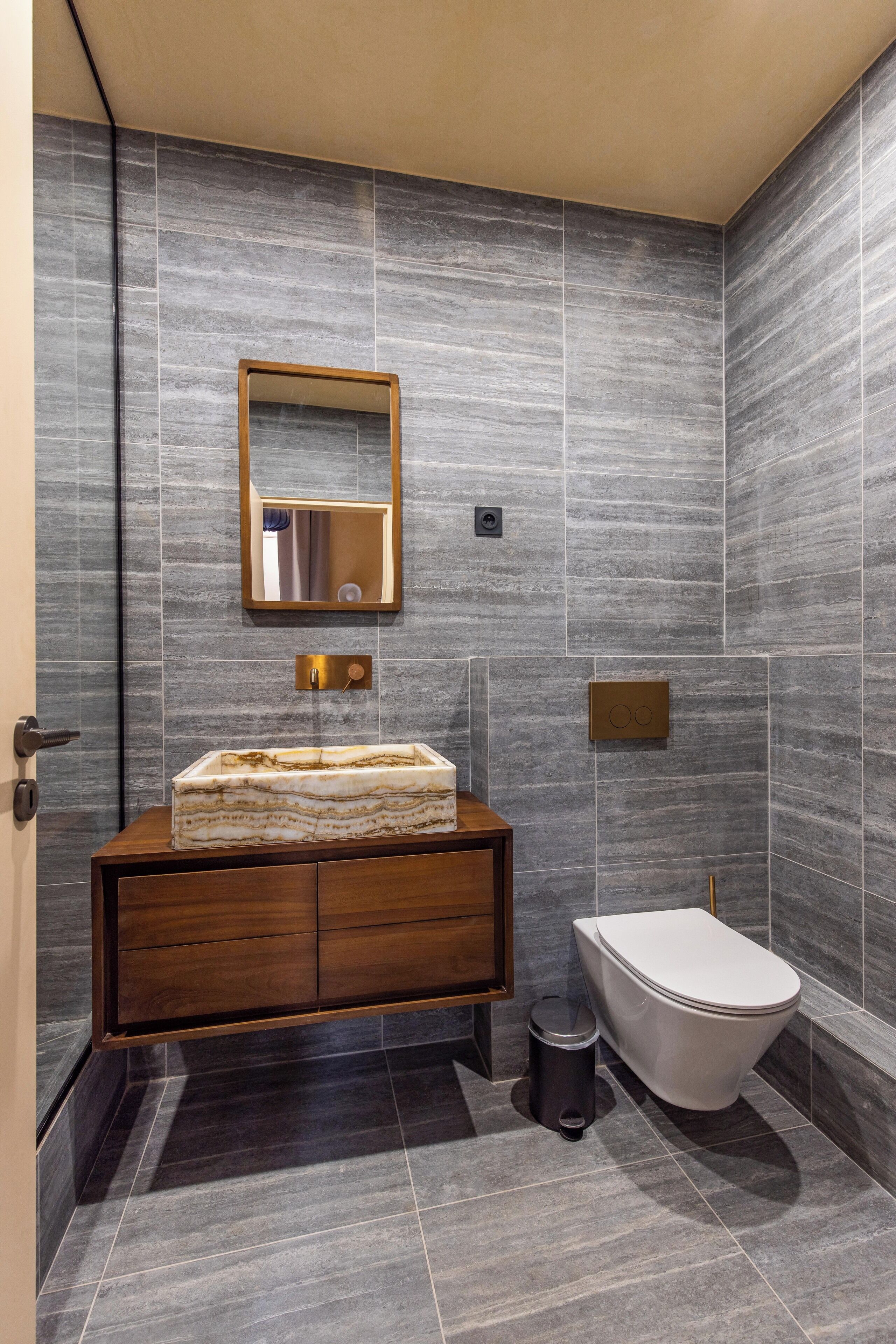 Un baño moderno con lavamanos de mármol, tocador de madera y un inodoro.