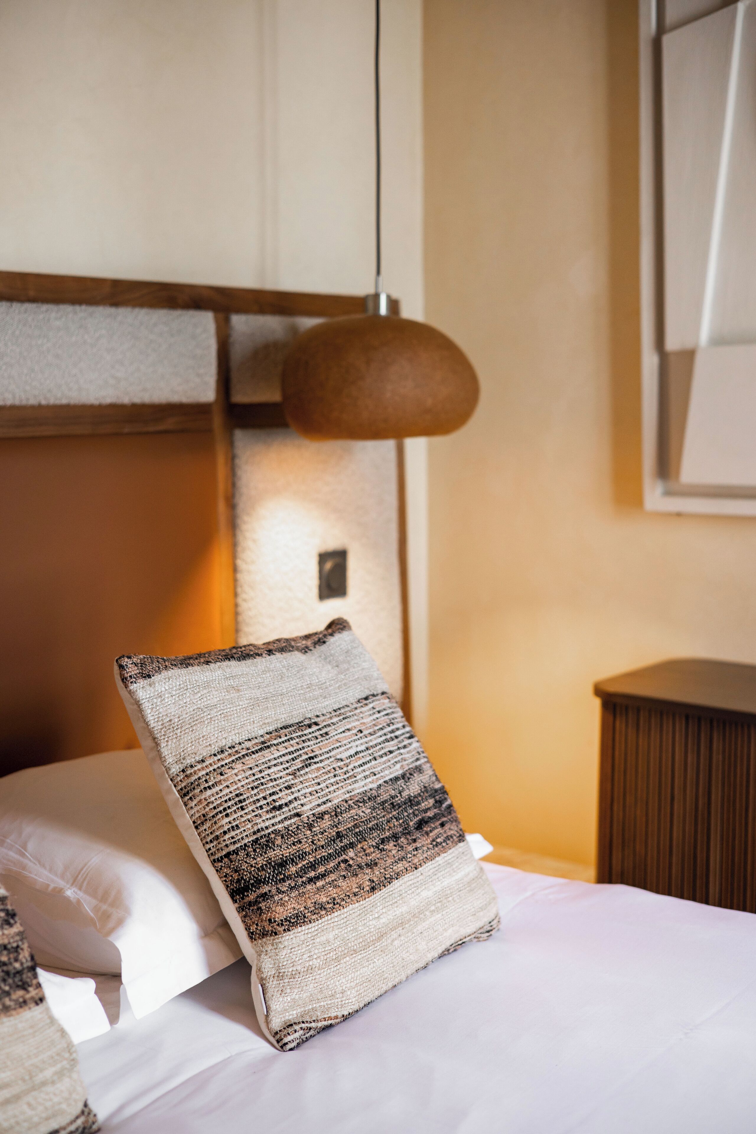 A neatly made bed with a patterned pillow, a bedside lamp, and a wooden nightstand.