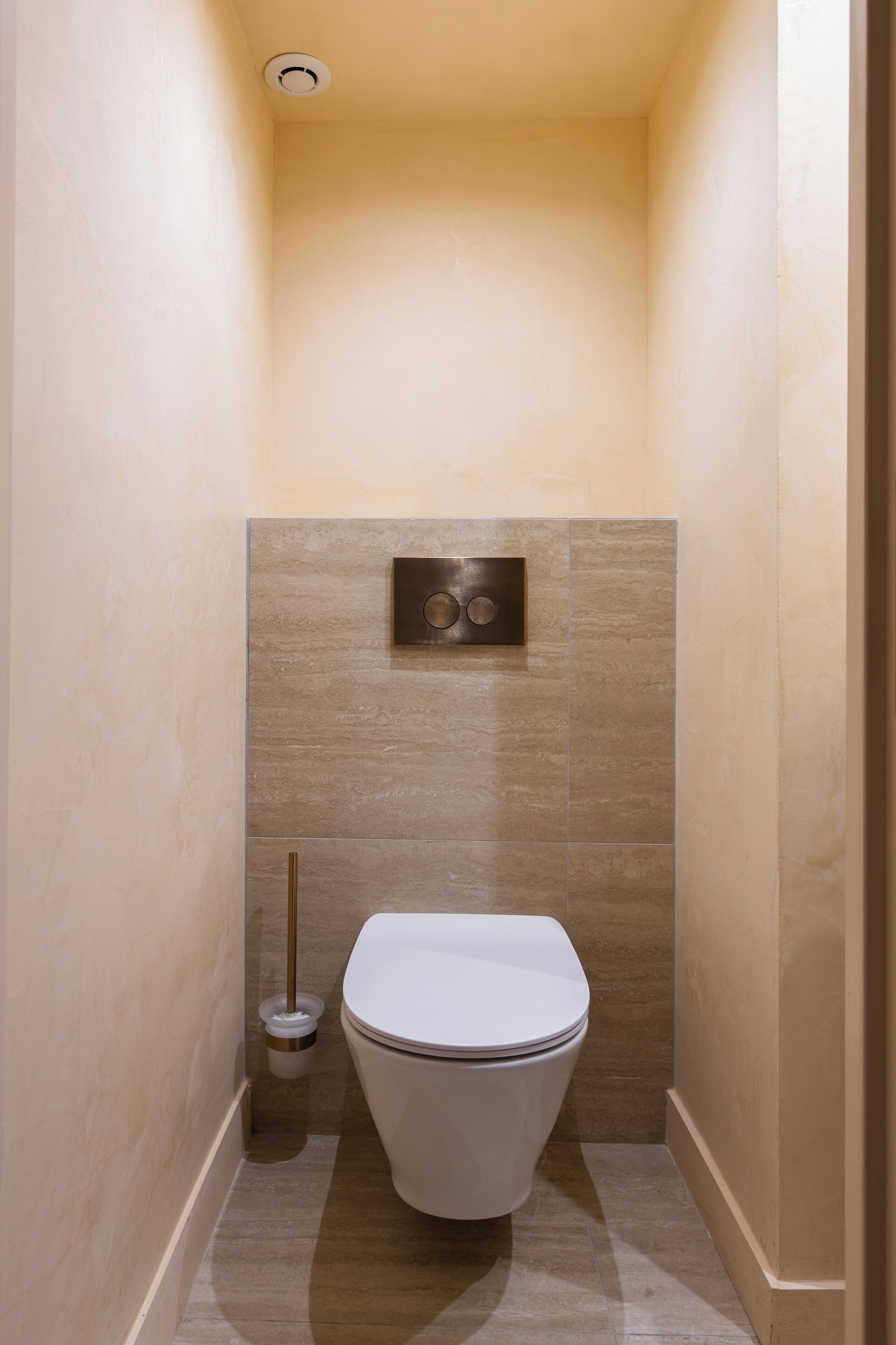 Een compacte, moderne badkamer met toilet, spoelhendel en een bedieningsknop op de muur.