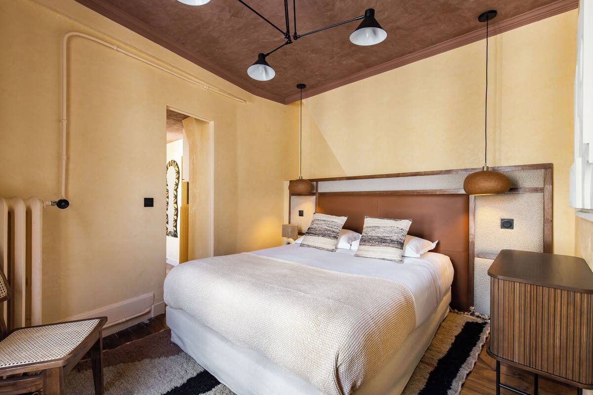 A bedroom with a large bed, a wooden headboard, a bedside table, and a chair.