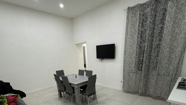 Une pièce moderne et bien éclairée, avec une table et des chaises, un téléviseur à écran plat fixé au mur et un rideau à motifs.
