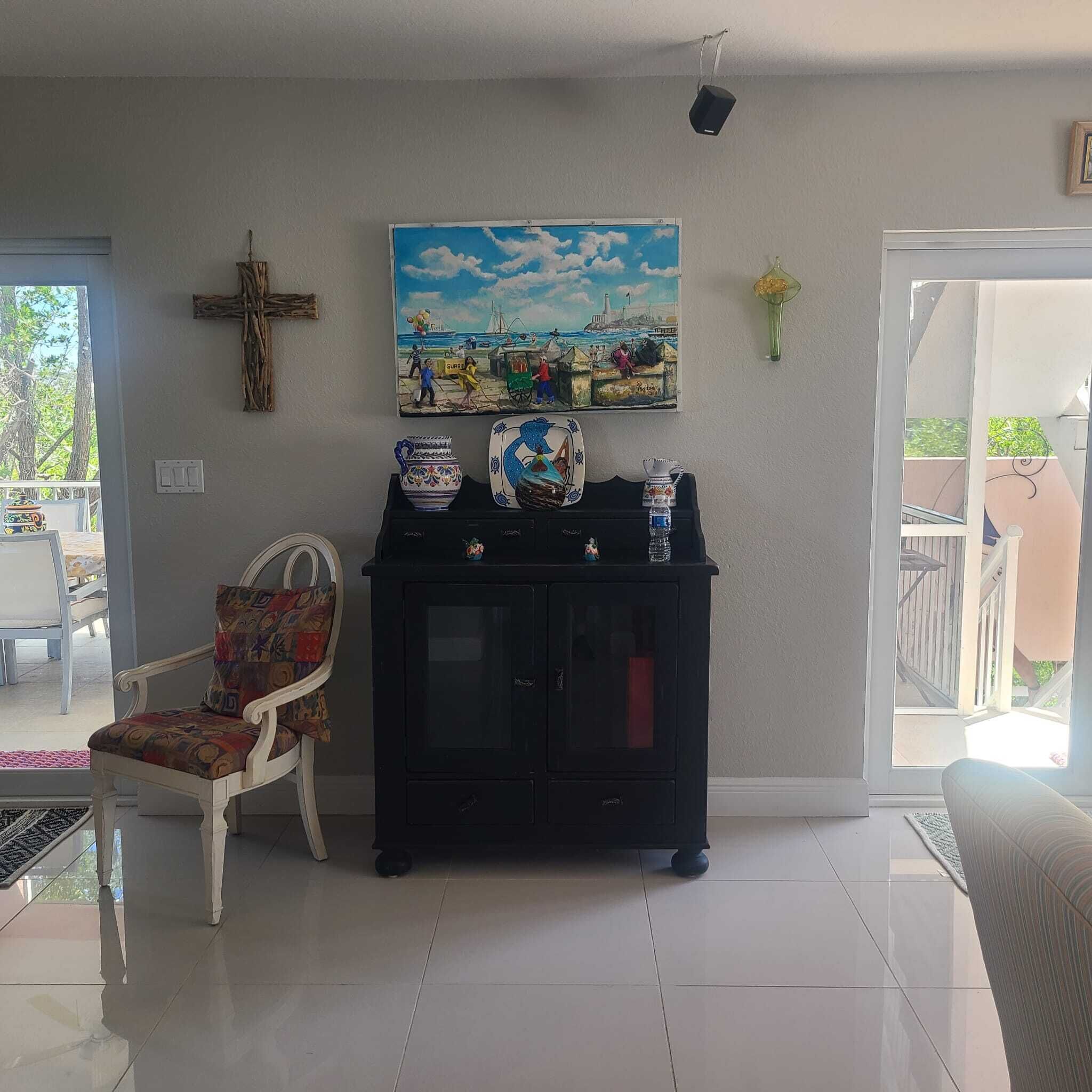 Una sala de estar con un mueble negro, una silla, un cuadro y una cruz en la pared.