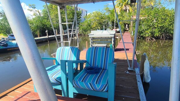 A covered deck with two striped chairs and a table, surrounded by water and greenery. - Waterfront private Key Largo Oasis House, with a Boat Dock (Key Largo)