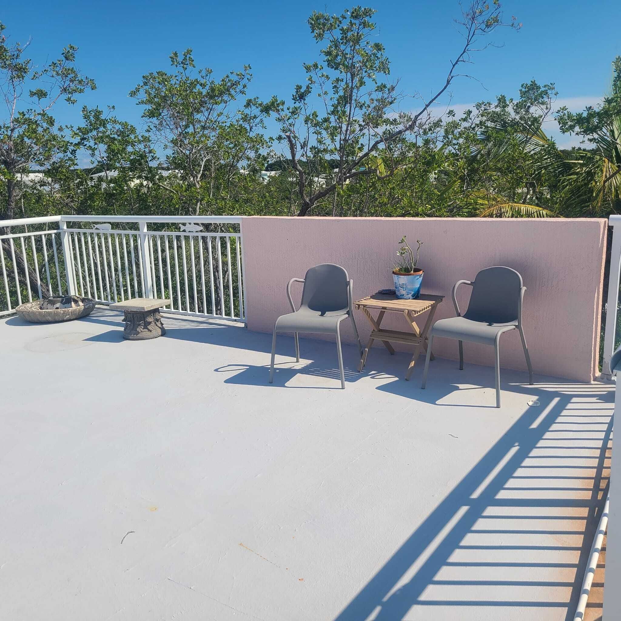 Un patio exterior con dos sillas y una mesa, una jardinera de piedra decorativa y una barandilla blanca.